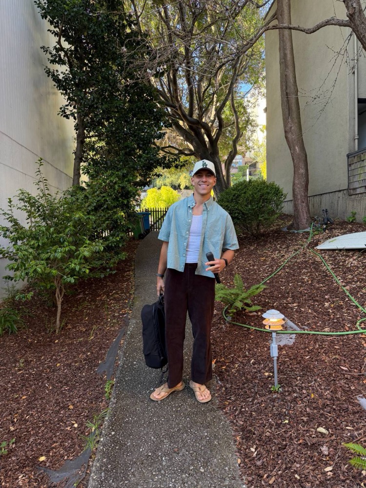Jaxson standing on a garden walkway in a green shirt and brown cords, holding a mic